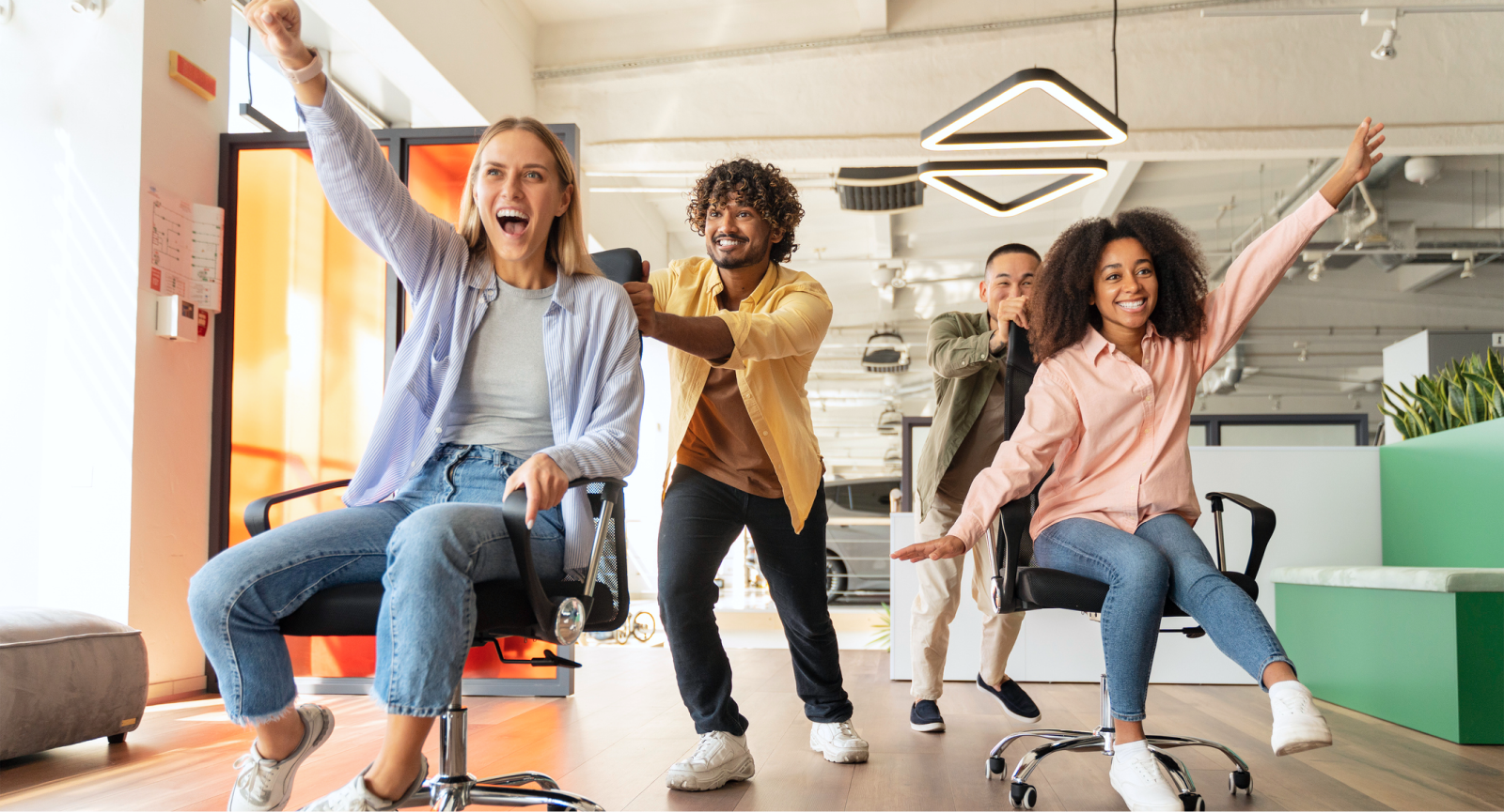 Coworkers laughing and pushing each other on office chairs in a bright office space