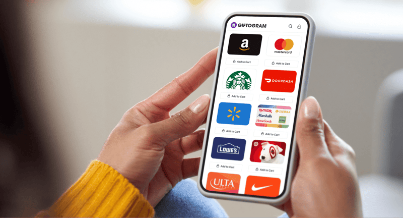 Person holds a phone displaying the Giftogram platform with gift card logos like Amazon, Starbucks, and Target, for employee recognition.