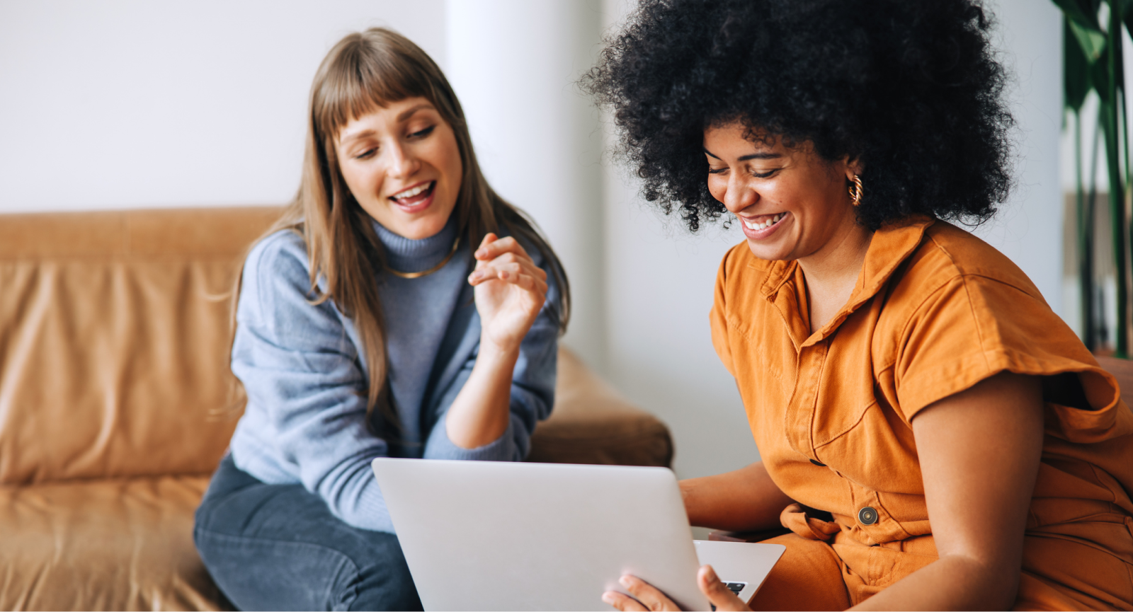 Two women smiling and collaborating on a laptop in a casual office setting