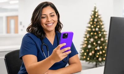 A smiling nurse checking her phone at a hospital desk decorated for the holidays