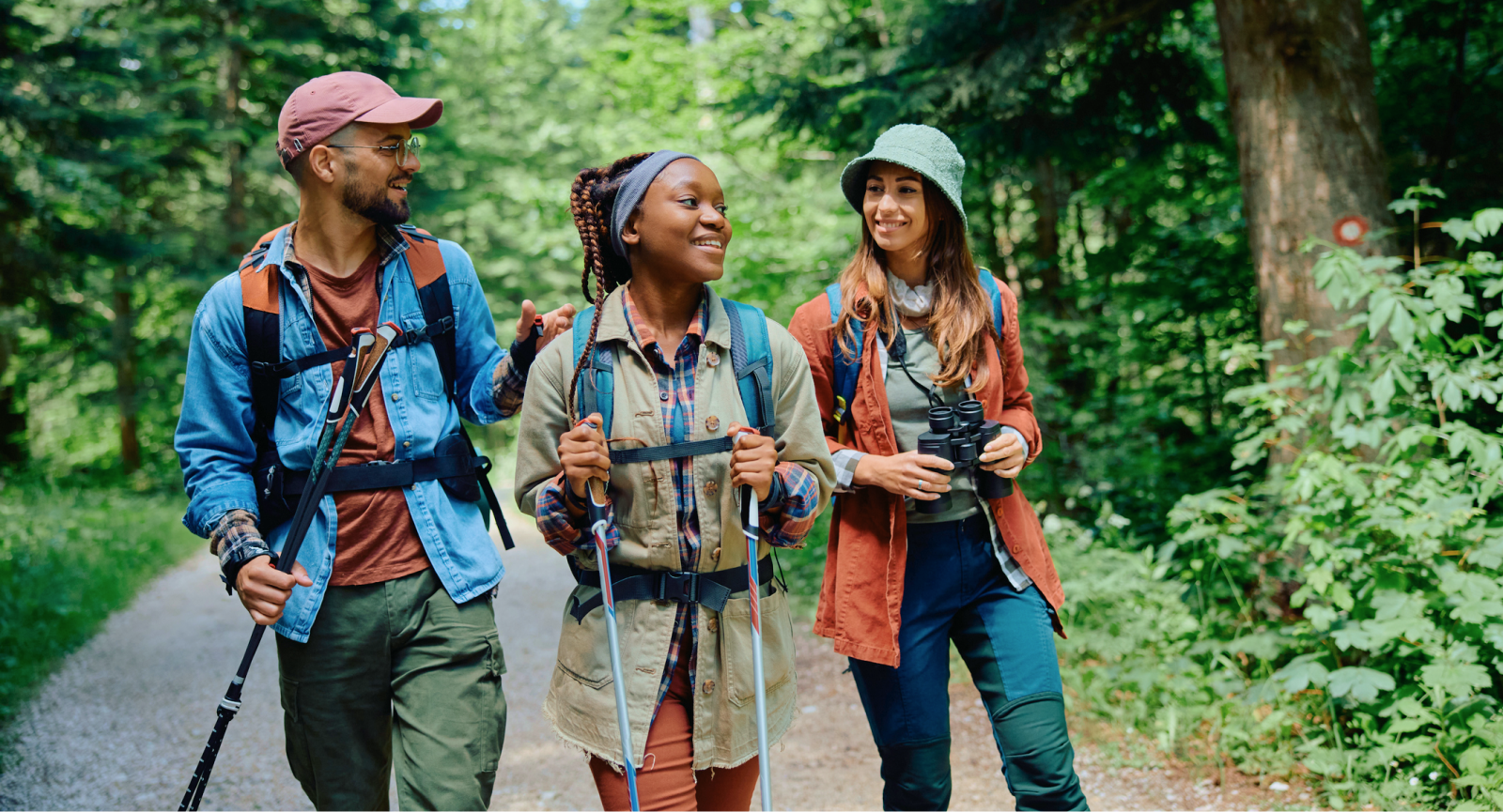 Diverse group of three hikers smiling on a forest path, promoting employee wellness and recognition.