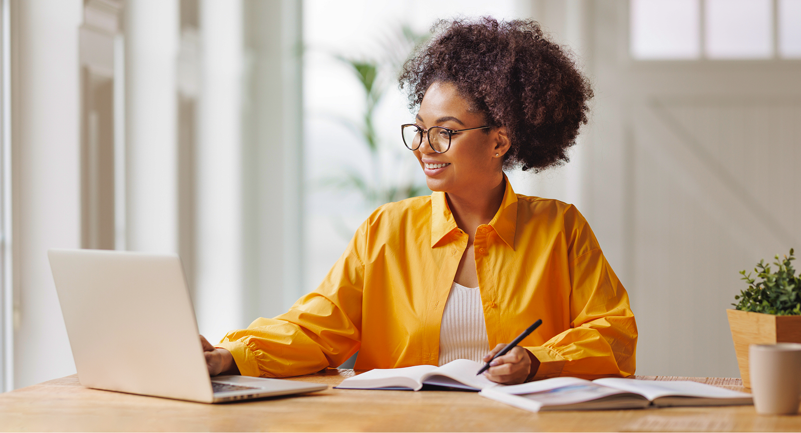 Smiling woman working at a laptop and writing in a notebook, strategizing business incentives.