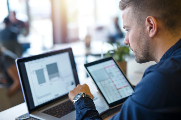 Man intently reviewing data on a tablet and laptop, managing Giftogram reward programs.