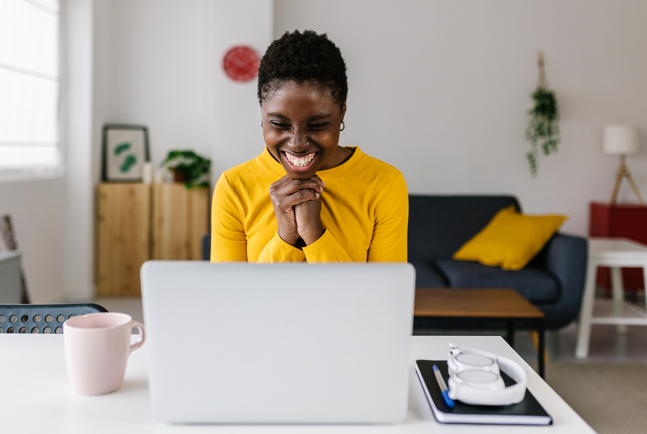 Happy woman smiling at laptop screen, hands clasped, reflecting the impact of employee recognition.
