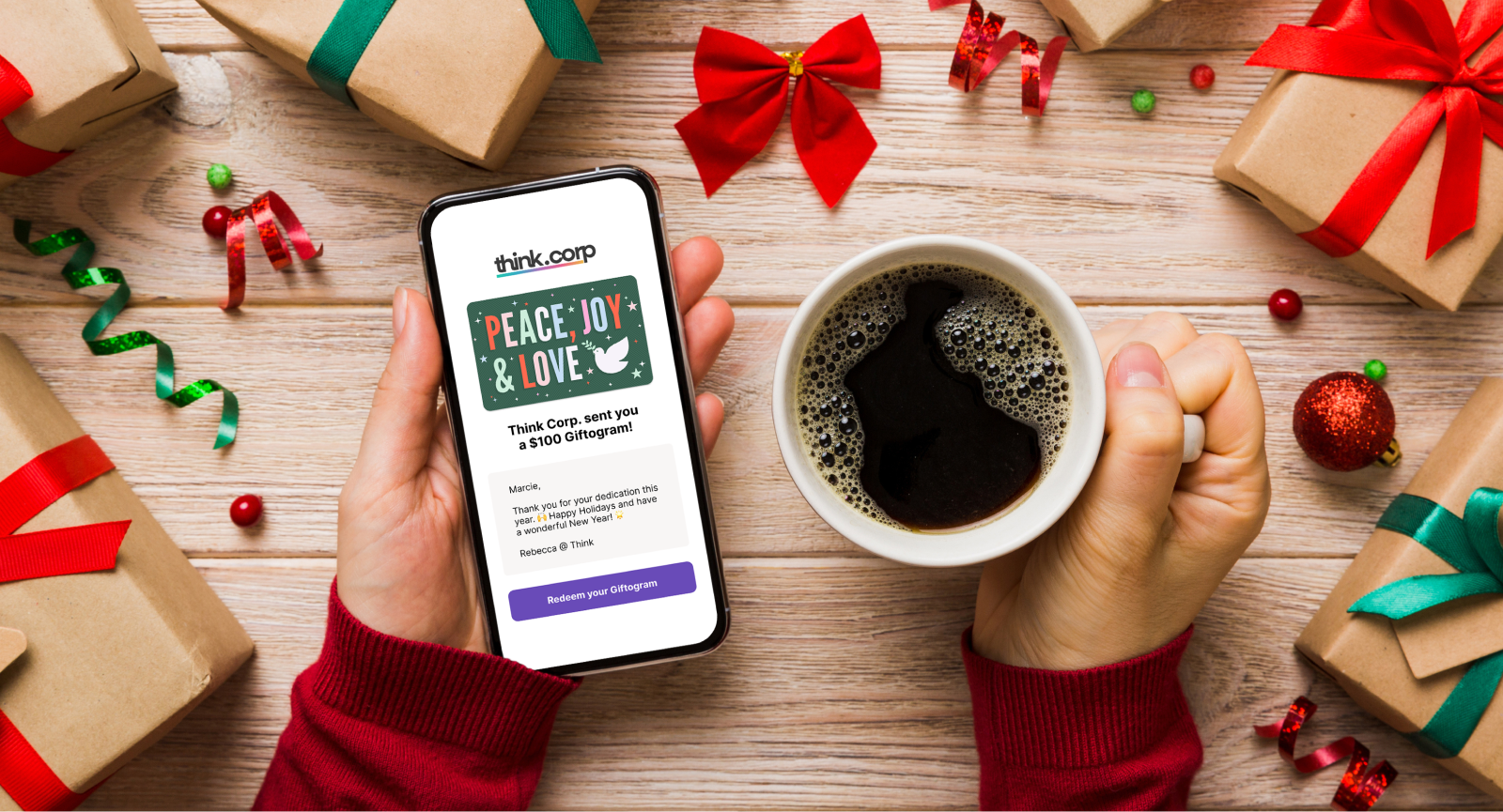 Hands holding a phone displaying a holiday Giftogram for employee appreciation and a coffee, surrounded by festive gifts.