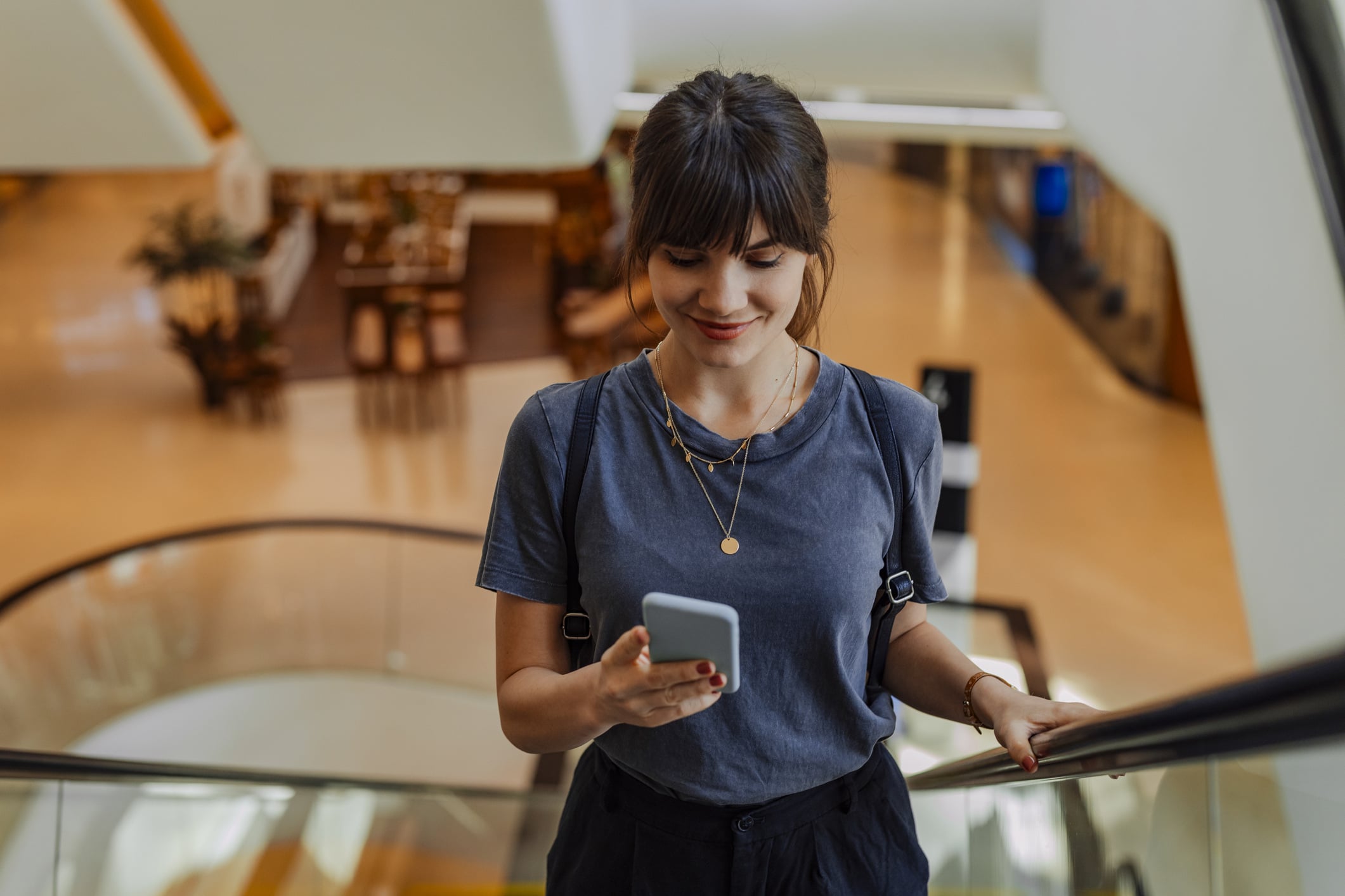 Woman smiling while checking her phone on an escalator, symbolizing the convenience of digital gift cards.