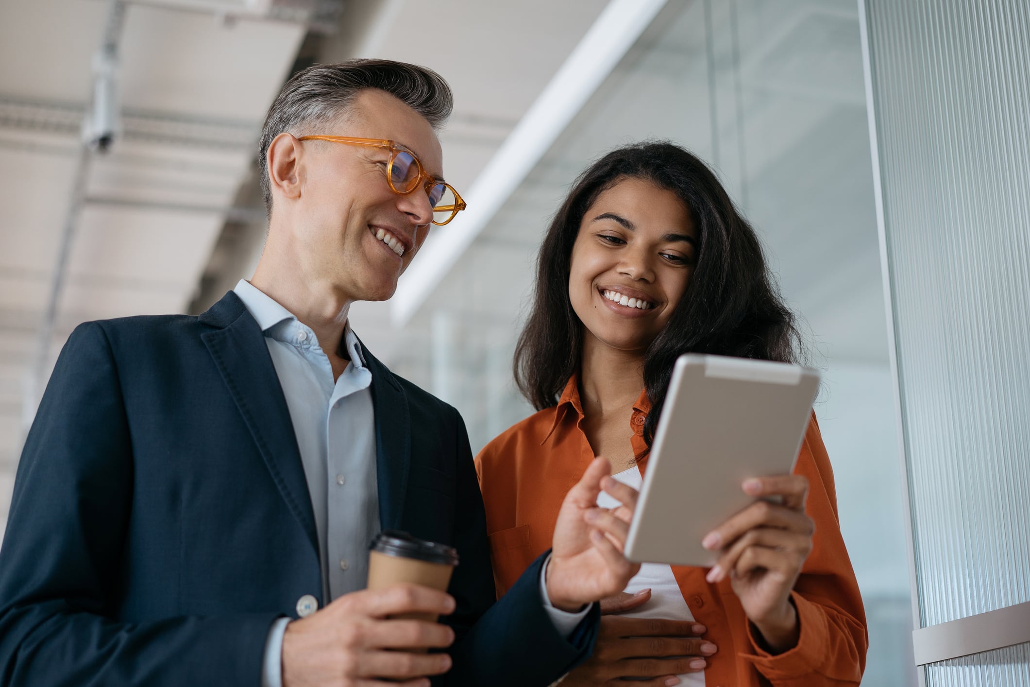 Two smiling colleagues in an office review a tablet, likely discussing ways to use Giftogram to improve employee recognition.