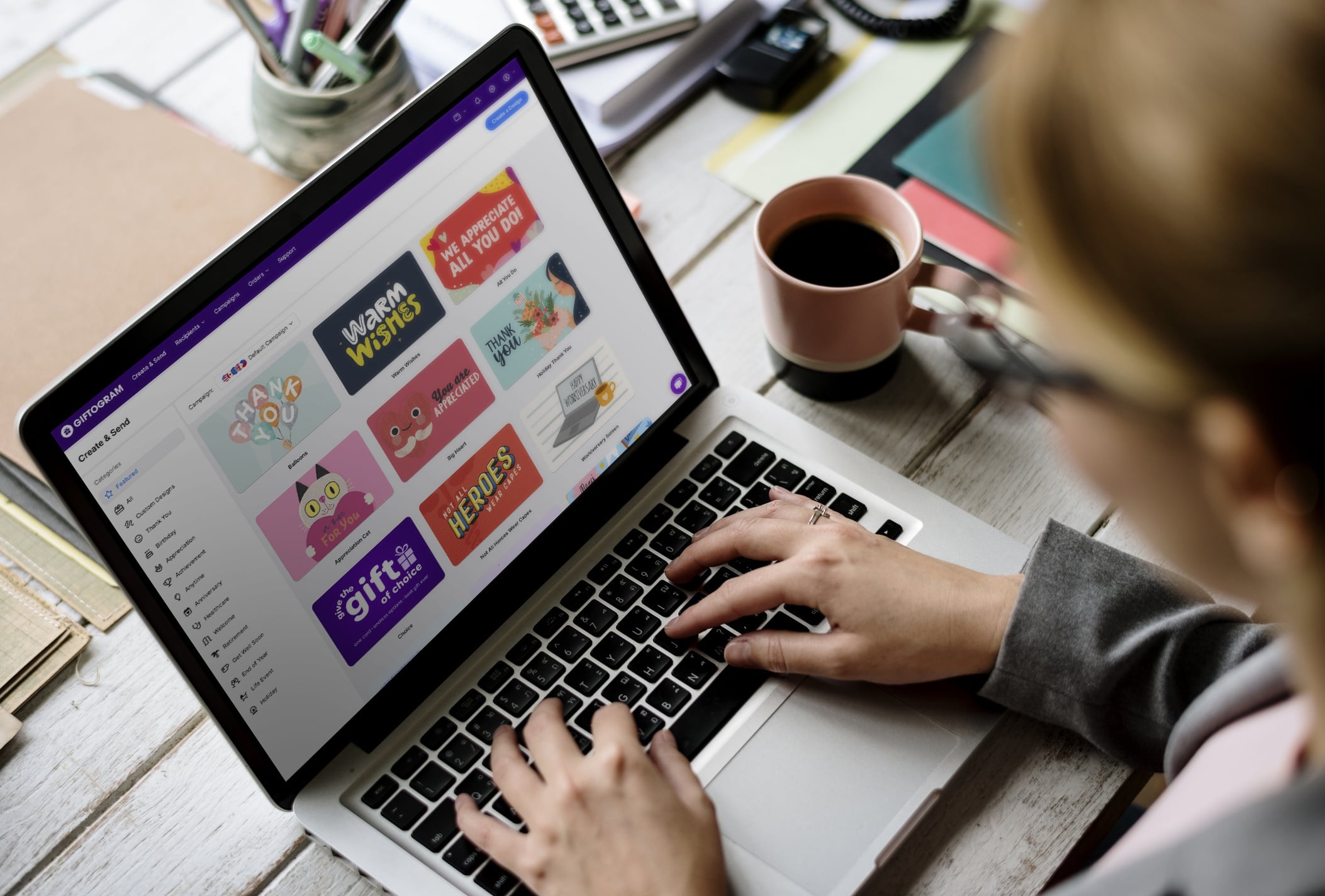 Person typing on laptop, selecting gift card designs on Giftogram's platform, like 'We Appreciate All You Do!', for employee recognition.